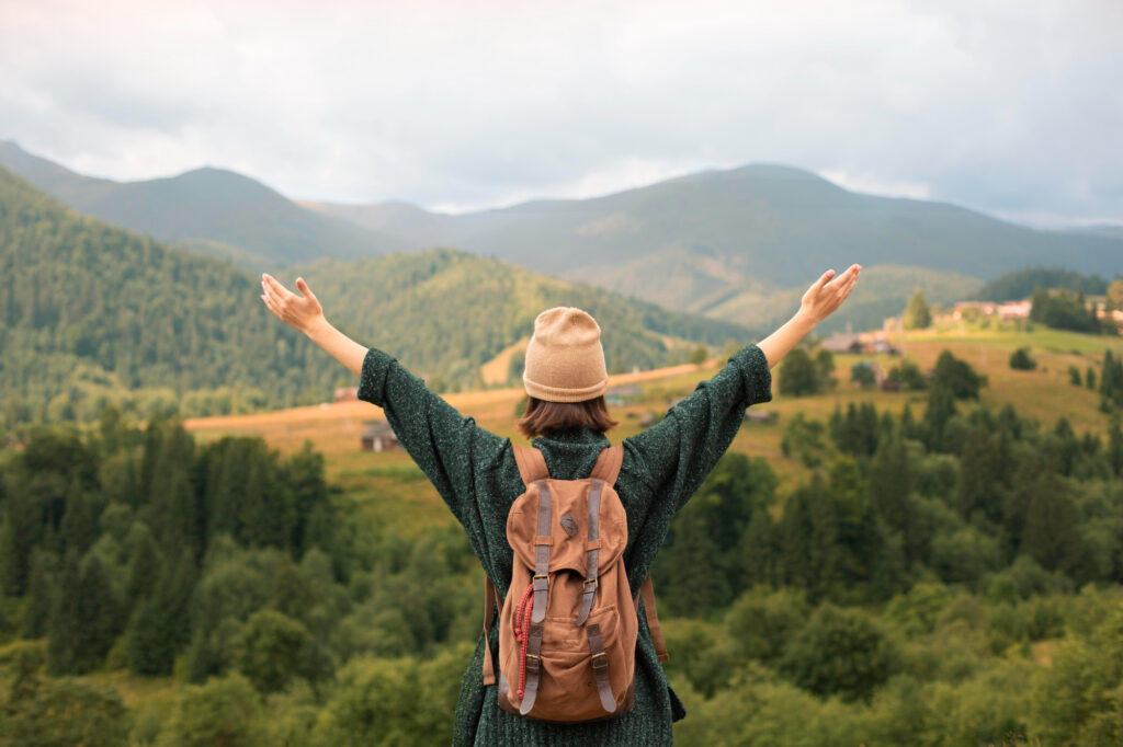 A picture showing a girl wearing a cream color hat and cream color bag in a joy full mood looking at greenery Infront of her.