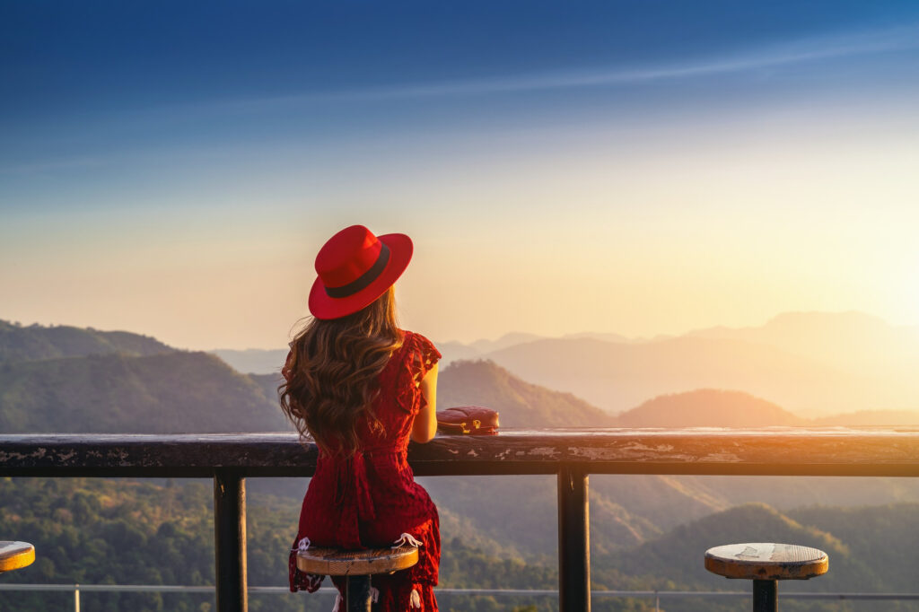 A landscape showing a girl with red dress and red hat looking at sunrise .this picture refers to Solo travel advice blog