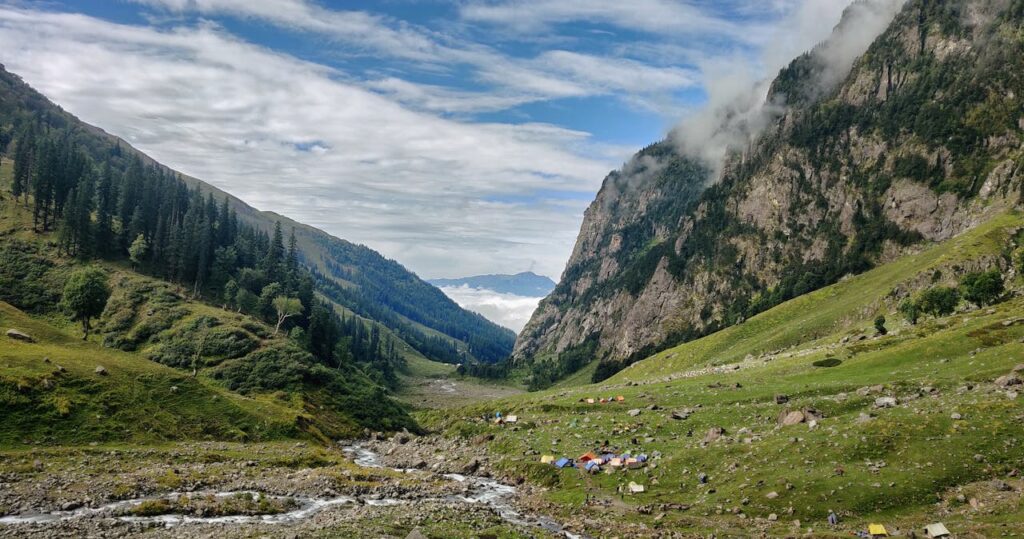 A landscape showing tourist camping  tents surrounded by large mountains, This image is used in the blog post Named as Budget tour for manali .