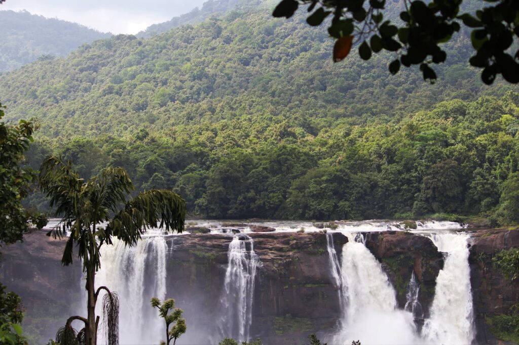A landscape showing waterfalls surrounded with dense forest and mountain.