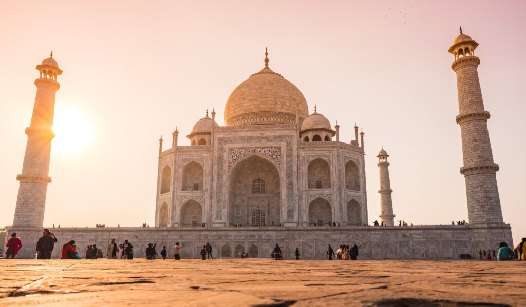 The Taj Mahal, a white marble mausoleum, features multiple elegant spires against a clear blue sky.