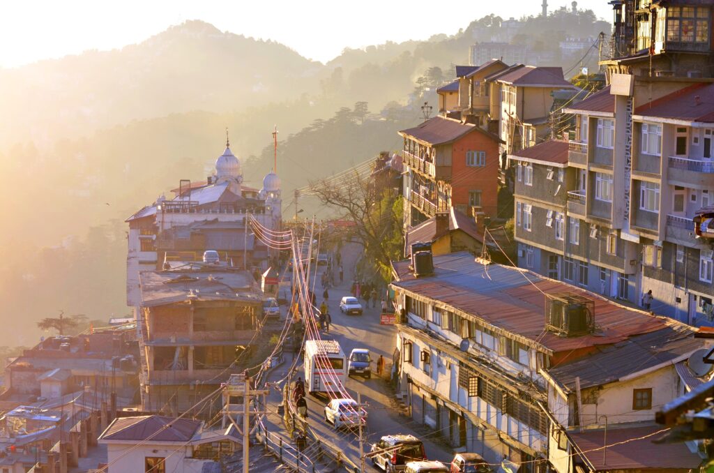 A bustling city street lined with various buildings and parked cars under a clear blue sky.